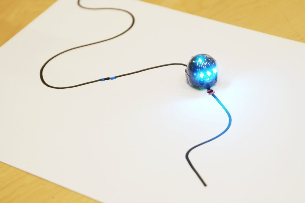 Little robot Ozobot following a path on a white sheet of paper drawn by a special black permanent marker.