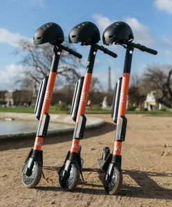 Three VOI electric scooters in a sand with helmets.