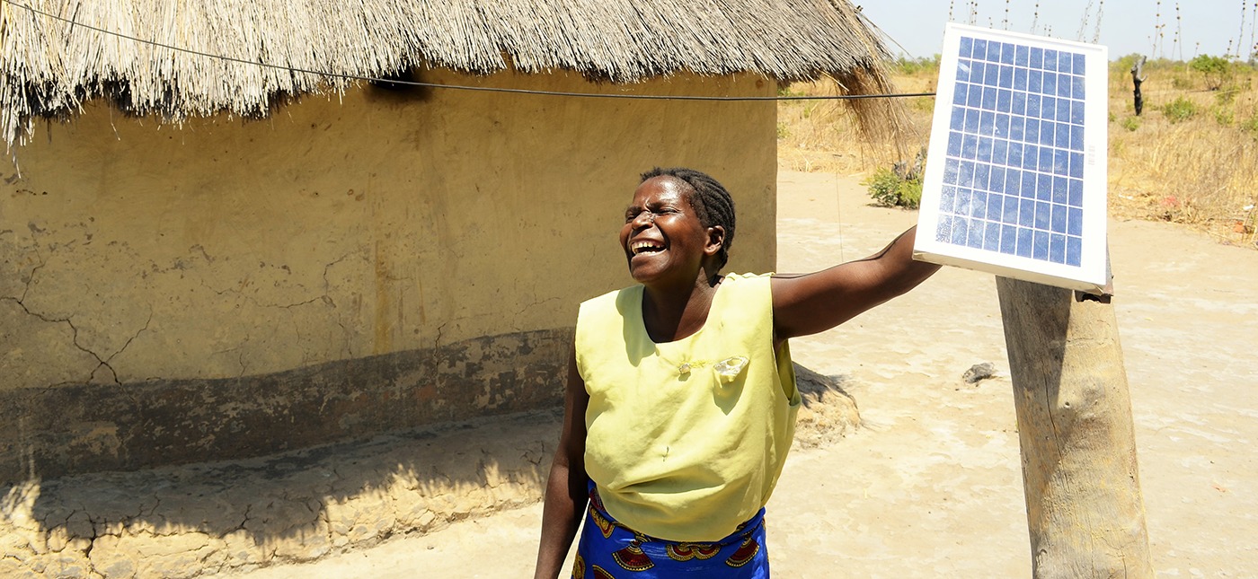 A woman from Africa is laughing and holding a solar panel crowdfunded thanks to Trine.